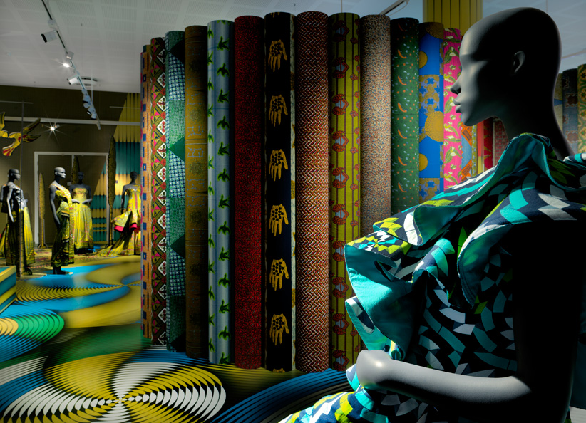 Mannequin in colourful outfit with various Vlisco fabrics in the background
