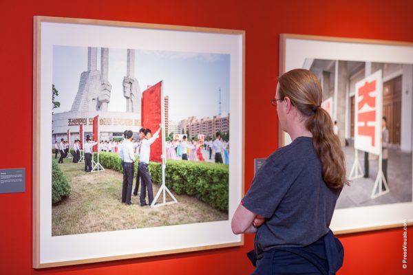 Mann mit Pferdeschwanz betrachtet ein Foto, das an einer roten Wand hängt