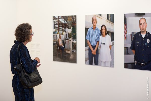 Eine Frau steht vor drei Porträtfotos